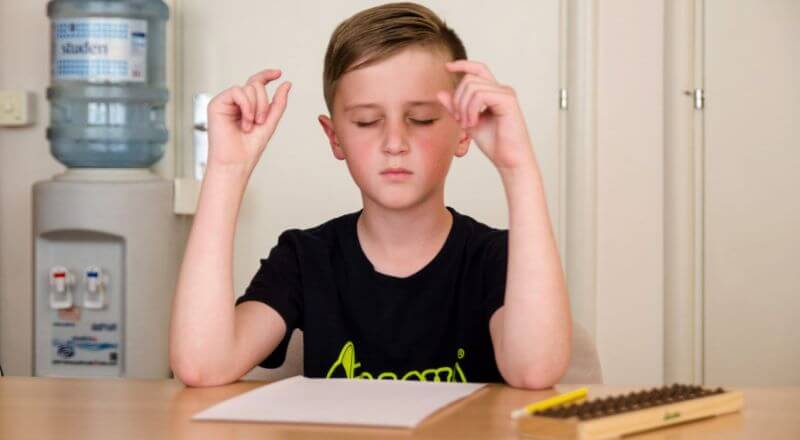 Dječak sjedi zatvorenih očiju, ispred sebe na stolu ima abakus i računa pomoću mentalne aritmetike.